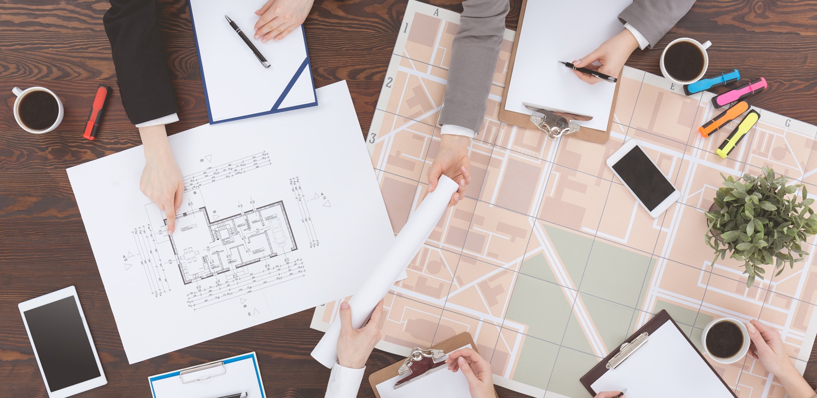 http://Architects%20working%20on%20plans%20around%20a%20wooden%20table